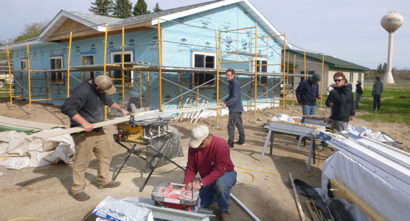 A group of people use tools while building a house during a service project with outward bound.